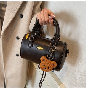 Detail of dark brown retro barrel bag featuring golden hardware and cute bear charm