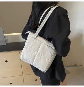 Quilted down shoulder bag in light grey shown worn by a model in a minimalist setting