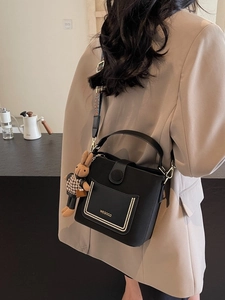Black bucket bag with wide strap and plush bunny charm worn by a person in a cafe