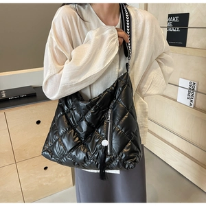 Detail of black quilted crossbody bag with tassel and patterned wide shoulder strap