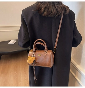 Brown leather boston bag shown with adjustable strap and cute plush bear charm detail