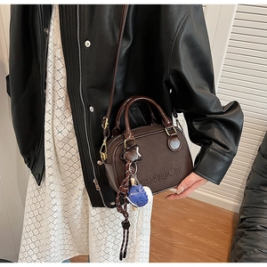 Détail du petit sac carré marron avec logo cœur embossé et breloque poupée peluche
