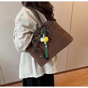 Detail view of large brown frosted suede tote bag with contrast leather and baseball charm