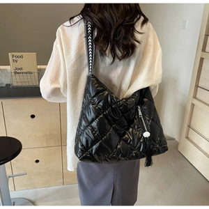 Detail of black quilted puffer hobo bag with patterned strap and flower tassel pendant