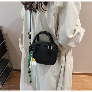 Détail du sac bandoulière noir avec pendentif baseball et cordon tressé vert élégant