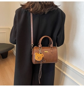 Brown leather Boston bag detail with plush bear charm and gold-tone hardware on model