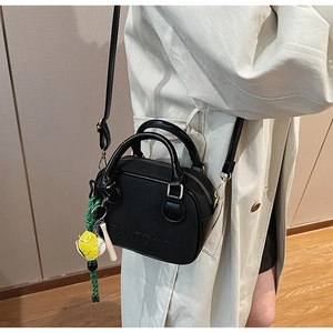 Détail du mini sac bandoulière noir avec logo embossé et pendentif tissé coloré