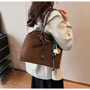 Detail of vintage brown suede tote bag with decorative baseball charm on the shoulder strap