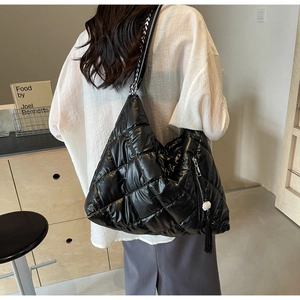 Detail of black quilted shoulder bag featuring a wide woven strap and fringe tassel charm