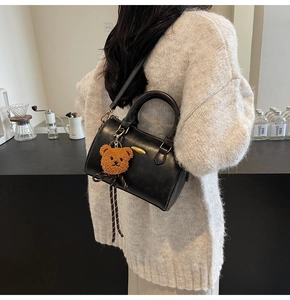 Detail of black Boston leather handbag featuring a cute brown plush bear charm and strap