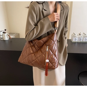 Detail of a brown quilted puffer tote bag with a floral tassel and ethnic woven strap