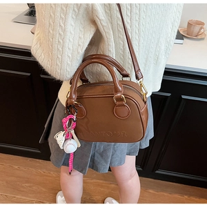 Sac Boston en cuir marron avec breloque de baseball porté sur un pull en maille blanc