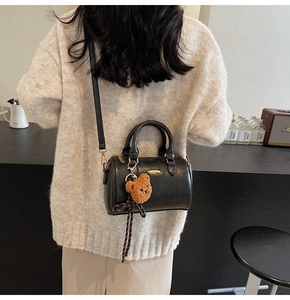 Detail of black Boston bag with teddy bear charm worn over a beige sweater in a cafe