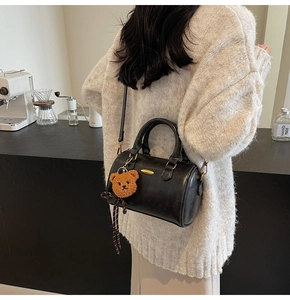 Close-up of black Boston bag with mini plush bear charm and adjustable strap detail