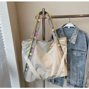 Détail de la bandoulière large SJCHAO sur cabas beige avec veste en jean en arrière-plan