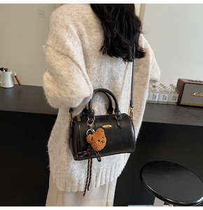 Chic black Boston bag with teddy bear charm shown cross-body on a model