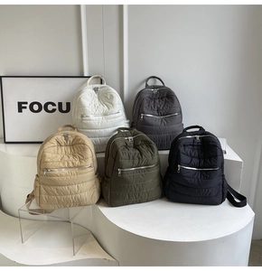Close-up of five quilted nylon backpacks in neutral colors with silver metallic zippers