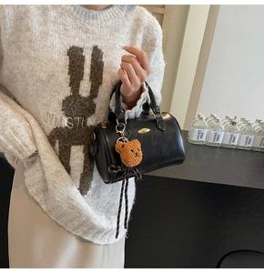 Detail of black leather cylinder bag with gold hardware and brown bear charm on model