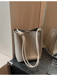 Minimalist grey lychee leather bucket tote bag with gold hardware on wooden display