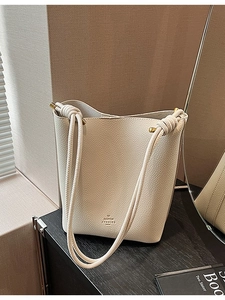 Chic beige lychee leather bucket bag with a knot handle and gold hardware detail