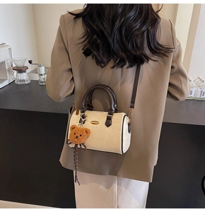 Chic cream bowling bag with brown trim and plush bear charm shown in a lifestyle setting