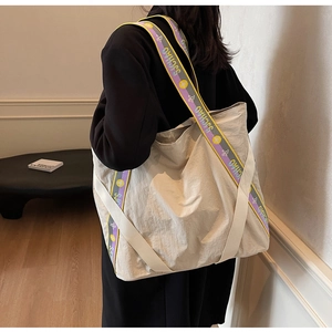 Grand sac cabas en toile beige avec bandoulière imprimée porté par un modèle