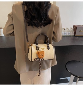 Detail of Boston-style cream cylinder bag featuring dark brown handles and a cute bear charm
