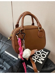 Petit sac carré marron avec poignée et pendentif tissé posé sur des livres