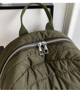 Detail of army green quilted backpack featuring dual silver zippers and nylon texture