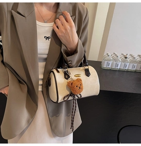 Detail of cream Boston bag featuring brown trim, plush bear charm and striped tassel detail