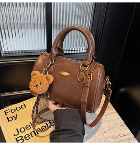 Detail of a brown Boston barrel bag with gold plaque and a plush bear keychain