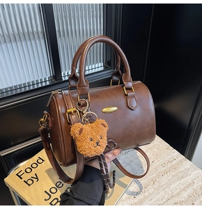 Detail view of coffee brown leather Boston bag with gold buckle and teddy bear charm