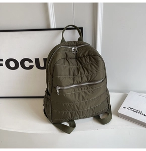Detail of olive green quilted backpack featuring metallic zippers and soft padded texture
