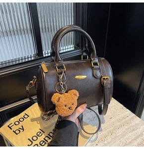 Detail of dark brown leather boston bag with golden hardware and cute bear charm