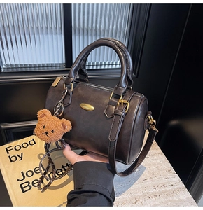 Detail of dark brown Boston barrel bag with plush bear charm on marble surface