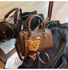 Detail of a brown leather barrel bag with gold hardware and a cute plush bear charm