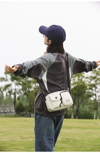 Outdoor view of a cream-colored minimalist crossbody bag with adjustable black nylon strap