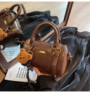 Detail of a vintage dark brown Boston bag with a cute plush bear charm on a wood floor