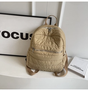 Detail of khaki quilted puffer backpack with horizontal stitching and silver zippers