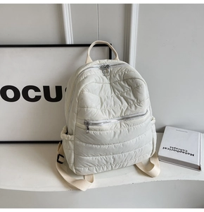 Detailed close-up of quilted cream white backpack featuring silver metal zippers and side pockets