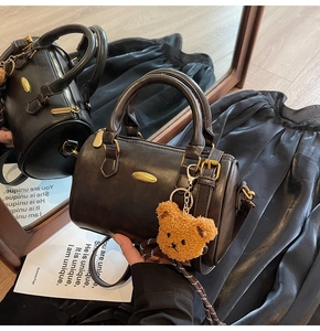 Detail of dark brown mini Boston bag with plush bear charm and striped webbing strap