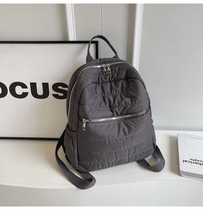 Detail of dark grey quilted backpack showing dual silver zippers and padded texture