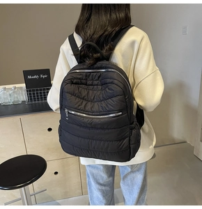 Detailed back view of model wearing a black quilted puffer backpack with silver zippers