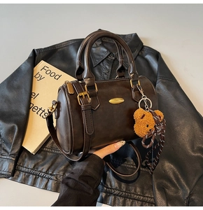 Detail of dark brown Boston bag with golden logo plaque and brown plush bear charm