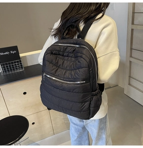 Rear view of model wearing a black quilted puffer backpack with silver metal zippers