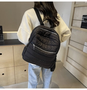 Detail of black quilted puffer backpack showing ripple stitching and silver metal zipper