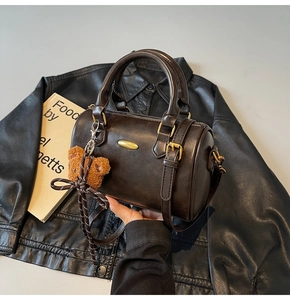 Detailed view of dark brown cylinder bag with gold hardware and cute teddy bear charm
