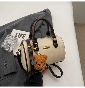 Detail of cream barrel bag with dark brown handles and cute plush bear charm decoration