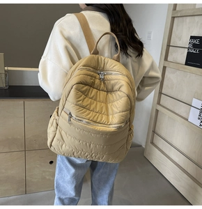 Detail view of the yellow quilted padded backpack with functional zipper pockets on model