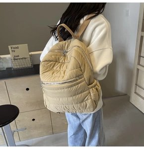 Detail of light tan quilted backpack featuring multi-zipper compartments and side pockets